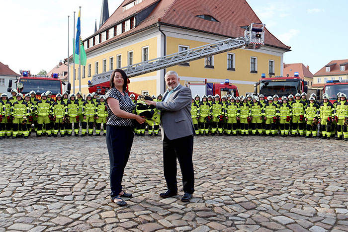 Übergabe Einsatzbekleidung durch Mandy Brußc, Mitarbeiterin der Weinhold Feuerwehrbedarf GmbH aus Kamenz, an den Bürgermeister Peter Mühle Übergabe Einsatzbekleidung durch Mandy Brußc, Mitarbeiterin der Weinhold Feuerwehrbedarf GmbH aus Kamenz, an den Bürgermeister Peter Mühle